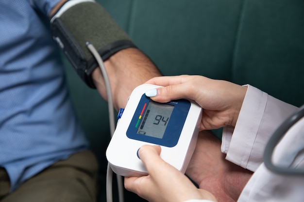 Um médico verifica a pressão arterial de um homem com um dispositivo eletrônico no sofá