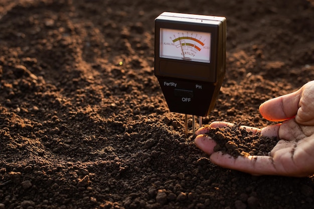 Um medidor de solo e as mãos de um agricultor estão pegando solo para plantar