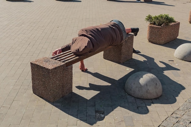 Um mendigo dormindo em um banco em uma rua urbana da cidade Dia Abuso Desespero Doente Mental Adormecido Viciado Mendigo Faminto Localização Alcoólatra Refugiado Calçada Parque Documentário