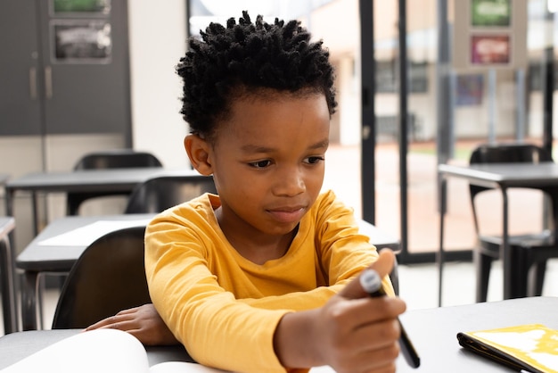 Um menino afro-americano com cabelos curtos e enrolados está concentrado em desenhar em uma sala de aula da escola