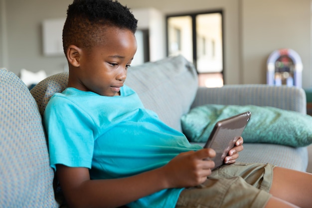 Um menino afro-americano usando um tablet digital enquanto estava sentado no sofá da escola