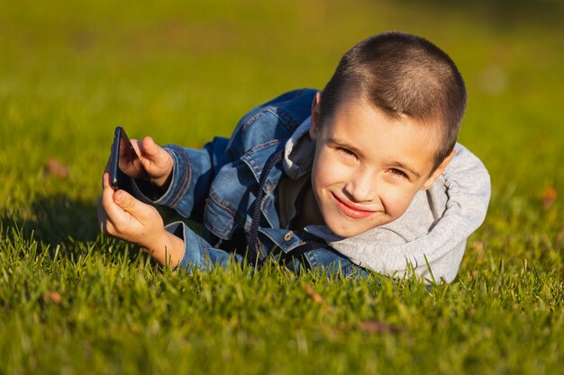 Um menino alegre brinca com um smartphone em um parque da cidade.