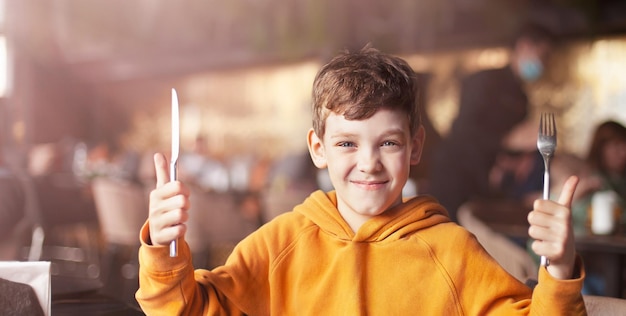 um menino alegre com talheres nas mãos está pronto para comer