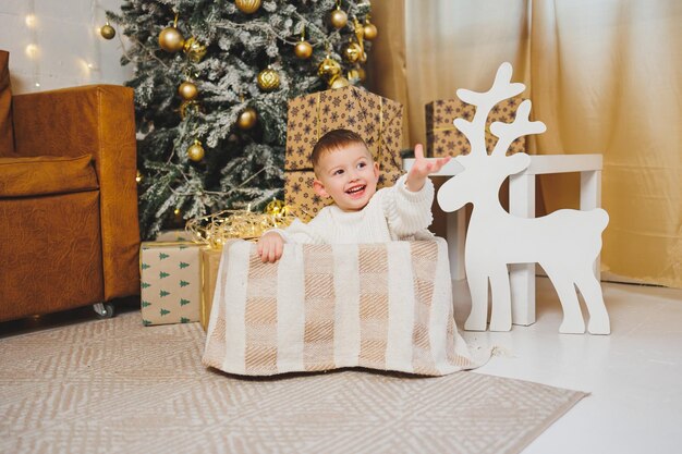 Um menino alegre de 23 anos está de pé perto de uma árvore de Natal cercado de guirlandas e Natal apresenta o conceito de um conto de Natal um feriado para crianças pequenas árvore de Natal