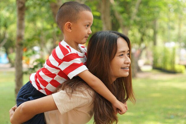 Um menino anda alegremente nas costas de sua mãe no parque