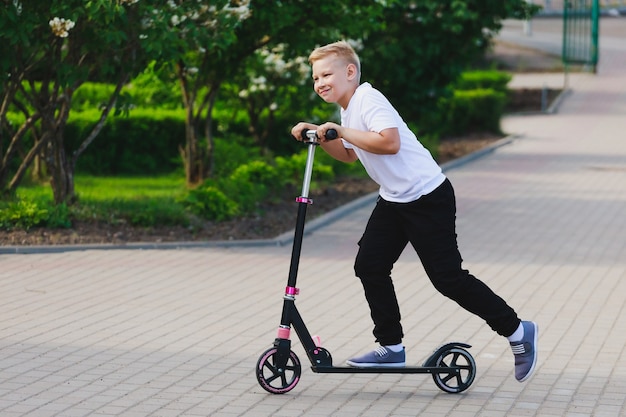 Um menino anda de scooter no parque no verão. Foto de alta qualidade