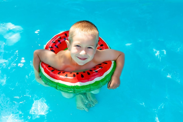 Um menino aprende a nadar em uma piscina azul com um círculo inflável vermelho brilhante