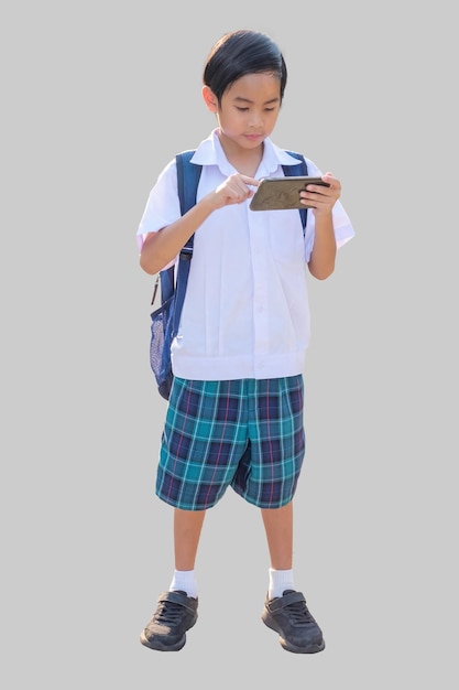 Um menino asiático de 10 anos de idade em uniforme escolar está de pé em seu smartphone