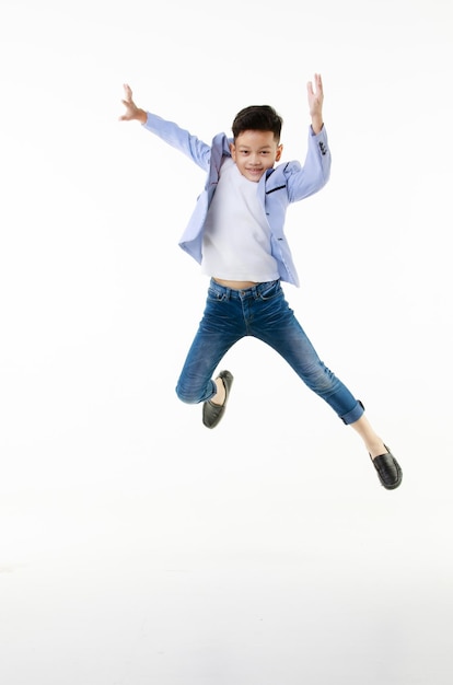 Um menino asiático de 10 anos em uma jaqueta casual está pulando de forma inteligente e feliz olhando para a câmera contra um fundo branco isolado