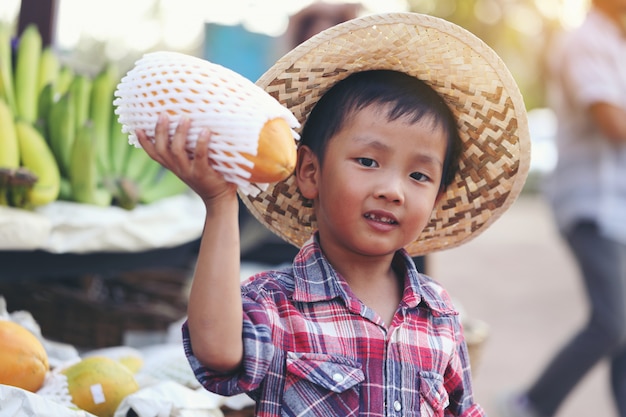 Foto um menino asiático mantém mamão esperando os clientes comprarem.