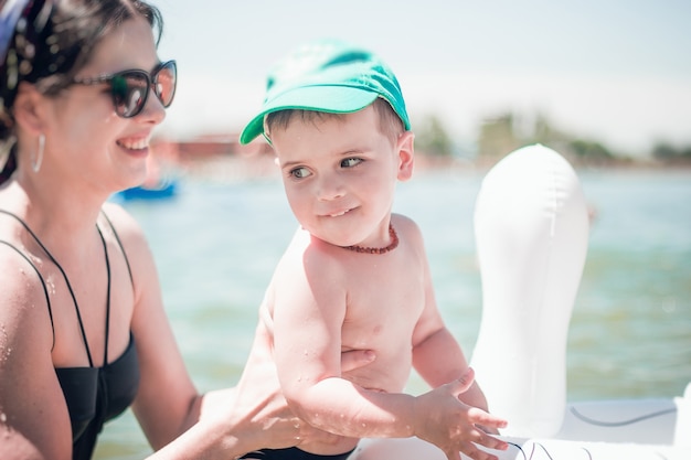 Um menino bonitinho com um boné de beisebol azul e uma jovem mãe atraente no mar com um anel inflável.