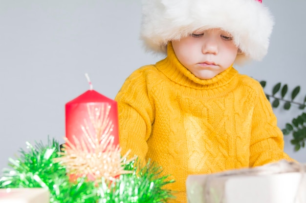 Um menino bonitinho com um suéter amarelo e um chapéu vermelho de Papai Noel com uma vela vermelha de Natal