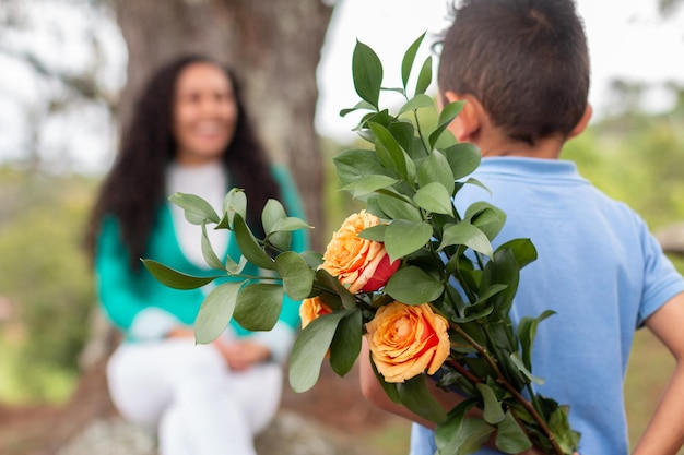 Um menino bonitinho esconde um buquê de rosas que preparou para sua mãe