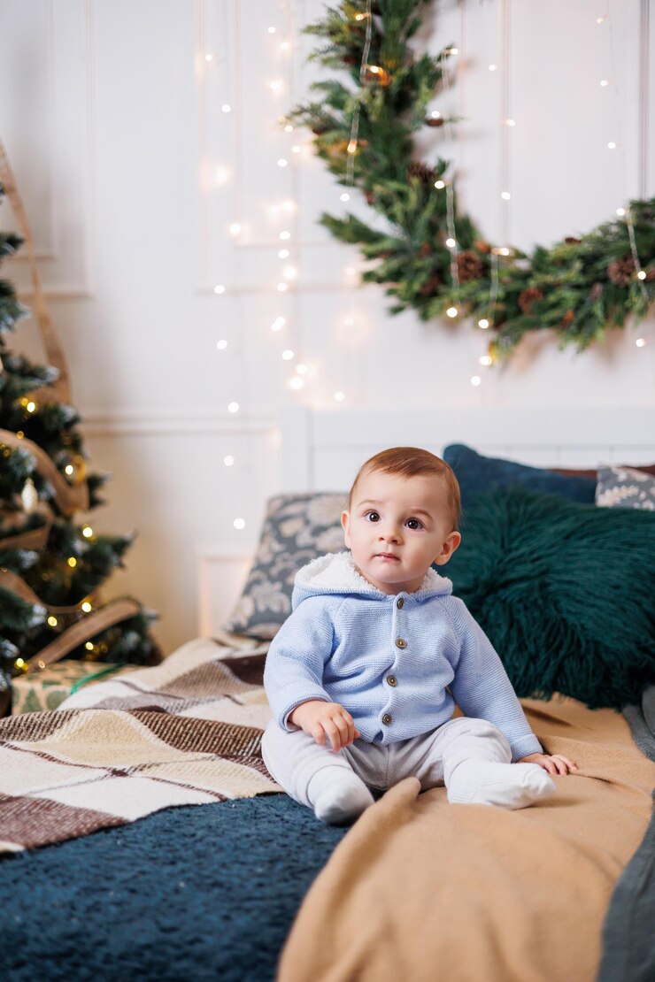 Um menino bonitinho está sentado em uma cama contra o fundo de uma árvore de Natal decorada decoração do quarto de Ano Novo