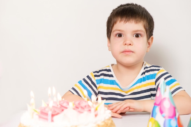 Um menino bonito comemora um aniversário, senta-se à mesa com um bolo com peneiras em chamas