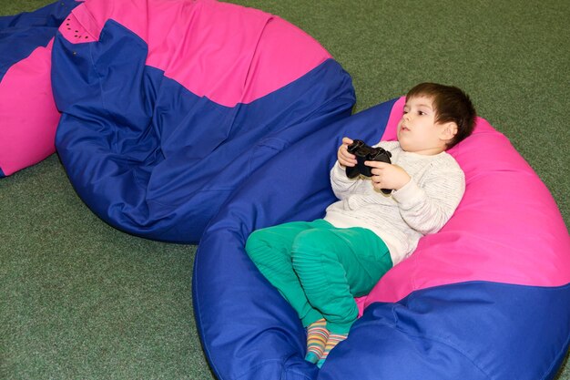 Um menino bonito de 4 anos joga um console de jogos segura um joystick nas mãos e desvia o olhar para um lugar para texto