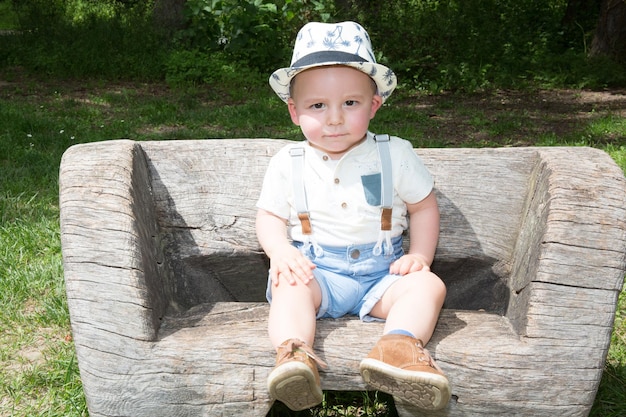 Um menino bonito de pé no banco do parque na tarde ensolarada