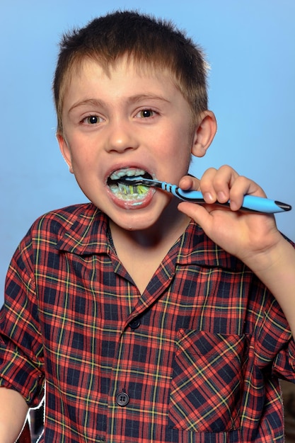 Um menino bonito de pijama escova os dentes com pasta de dente antes de dormir em um fundo azul