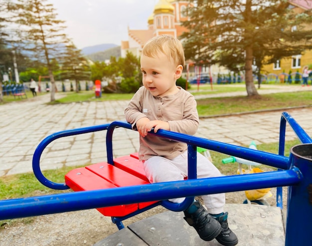 Um menino bonito de um ano e meio anda em um balanço no playground entretenimento infantil foco seletivo