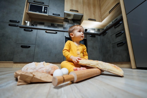 Um menino bonito de um ano está sentado na cozinha e comendo um pão comprido ou baguete na cozinha A primeira vez que uma criança come pão O pão é bom para as crianças