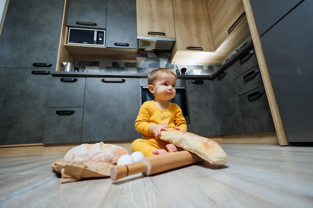 Um menino bonito de um ano está sentado na cozinha e comendo um pão comprido ou baguete na cozinha A primeira vez que uma criança come pão O pão é bom para as crianças