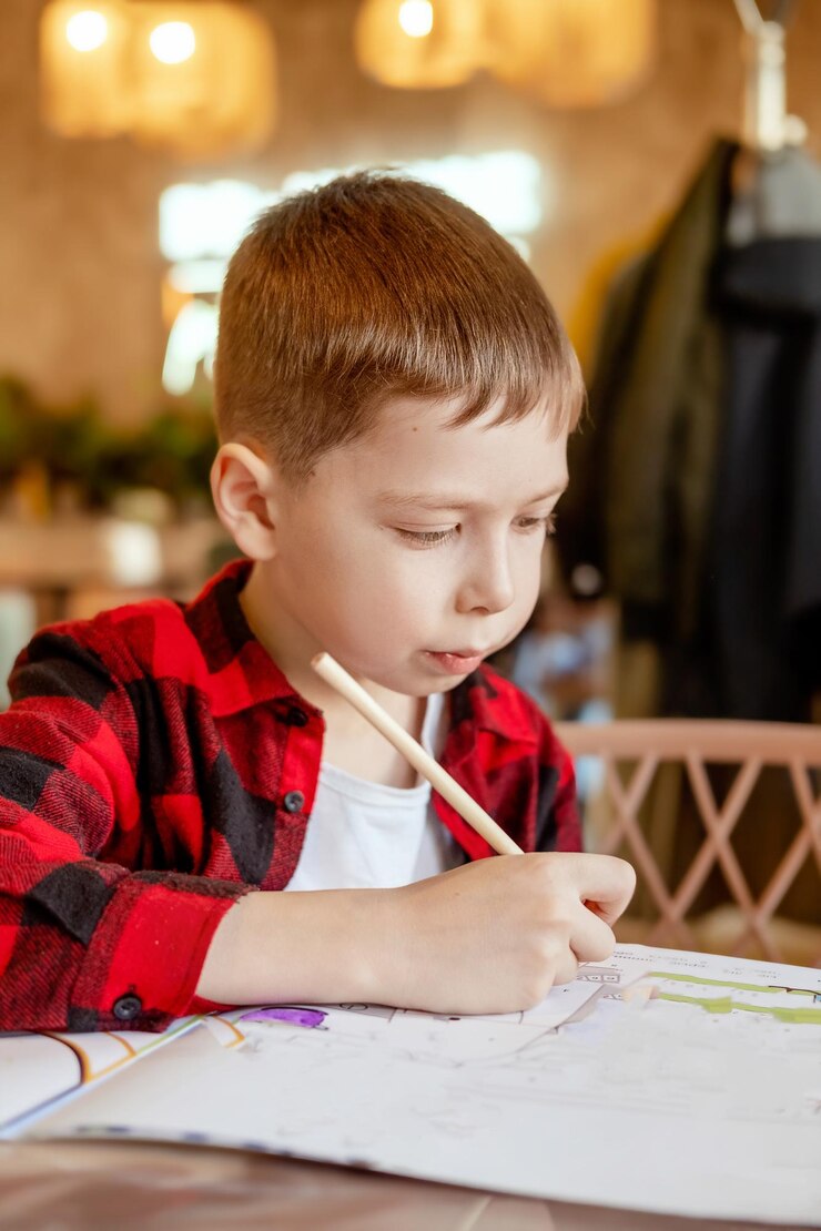 Foto um menino bonito desenha na mesa com um lápis esperando uma encomenda em um café o menino desenha