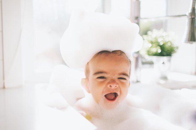 Um menino bonito e feliz a tomar um banho de espuma na pia da cozinha em casa