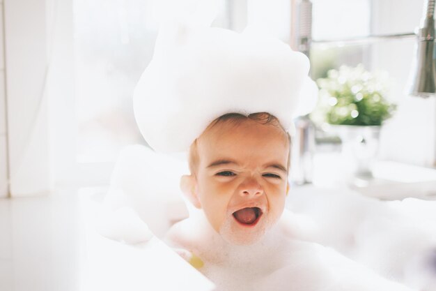 Foto um menino bonito e feliz a tomar um banho de espuma na pia da cozinha em casa