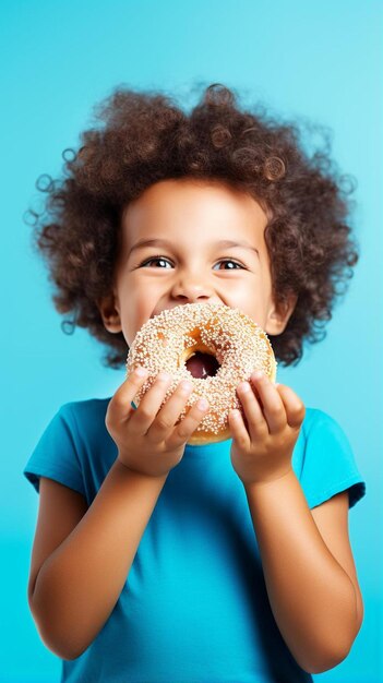 Foto um menino bonito e feliz está comendo um donut em uma parede de fundo azul. a criança está se divertindo com um donut saboroso.