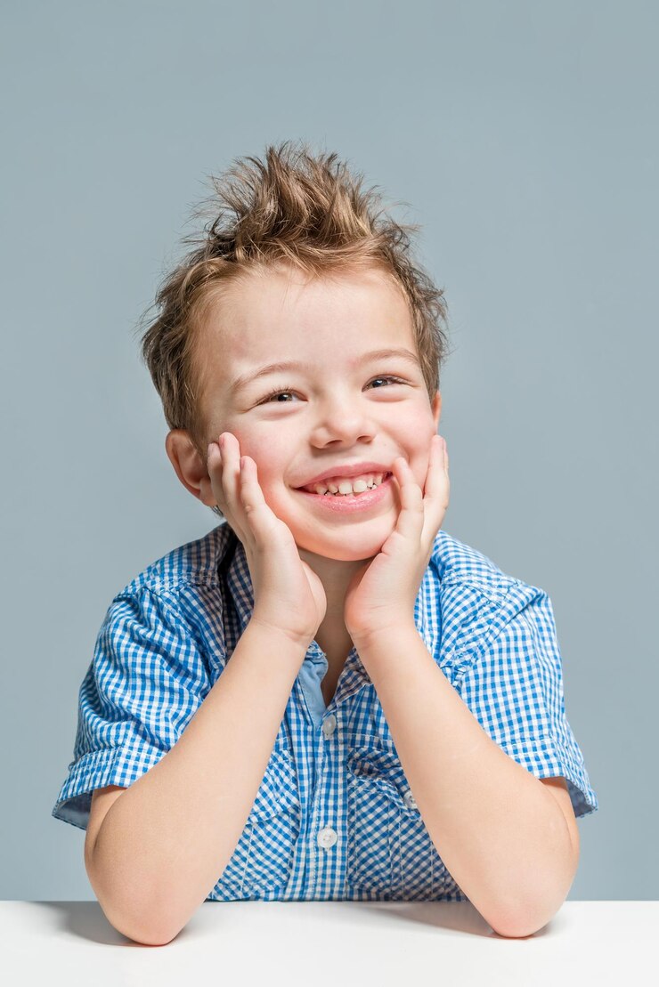 Foto um menino bonito e sorridente com uma camisa azul na mesa sobre um fundo cinza isolado