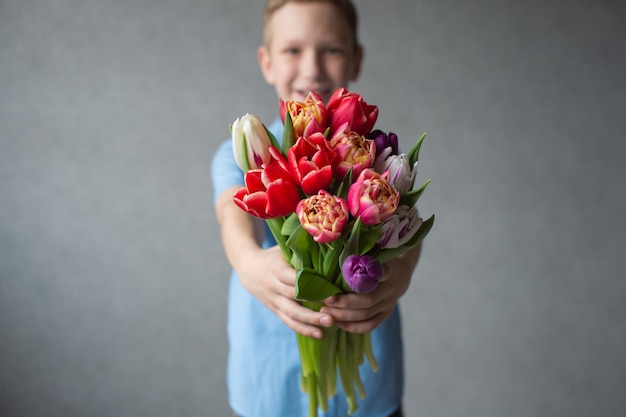 Um menino bonito em uma camisa oferece um buquê colorido de tulipas para a frente