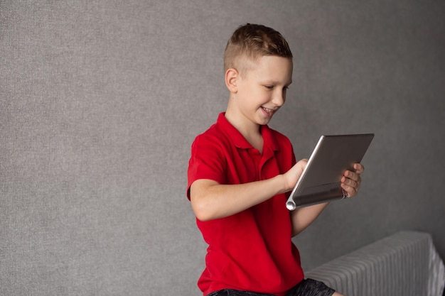 Um menino bonito em uma camiseta vermelha olha para um tablet