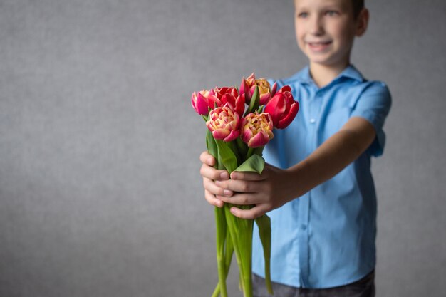 Um menino bonito estendeu as mãos com um buquê de tulipas para parabéns presente de dia das mães