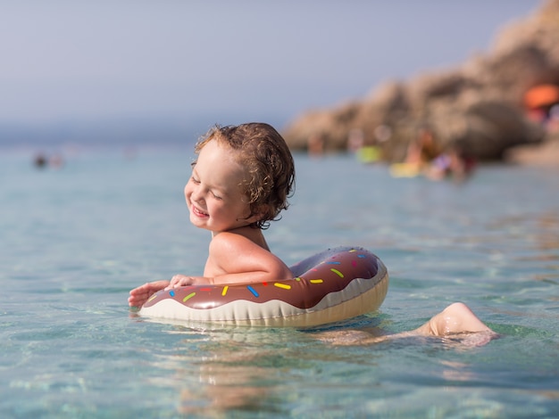 Foto um menino bonito, nadando no mar menino feliz brincando de nadar no mar com anel inflável. conceito de crianças de férias de verão