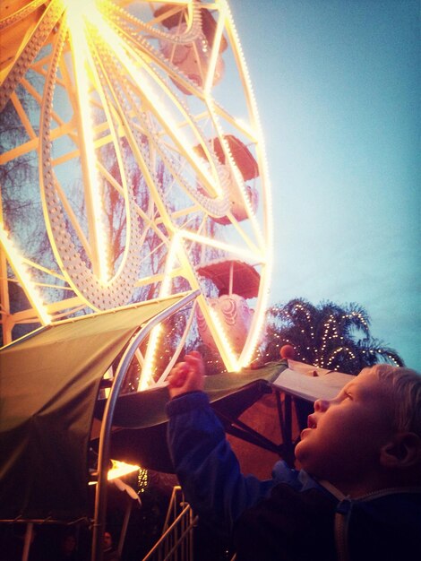 Foto um menino bonito olhando para uma roda gigante iluminada contra o céu ao anoitecer