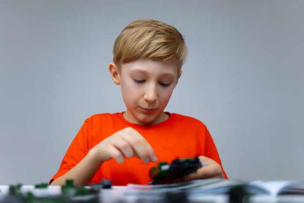 Um menino brinca com um construtor de plástico tem um modelo montado do construtor em suas mãos