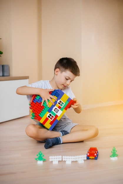 Foto um menino brinca com um kit de construção e constrói uma casa-grande para toda a família. construção de uma casa de família.