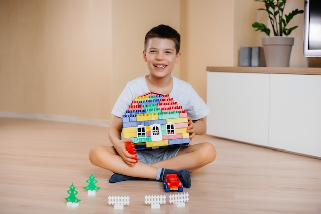 Um menino brinca com um kit de construção e constrói uma casa-grande para toda a família. Construção de uma casa de família.