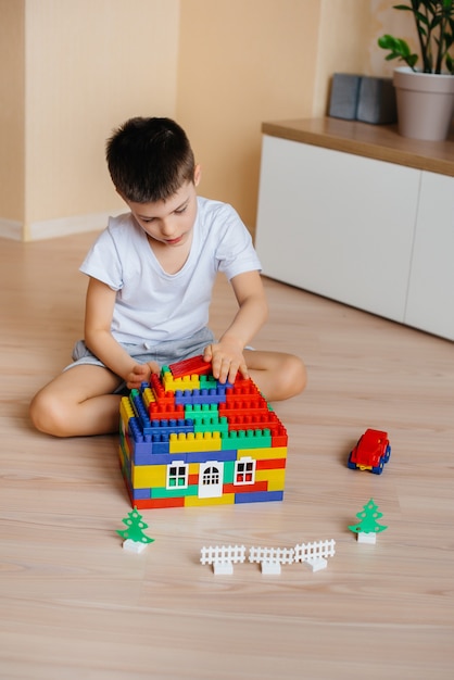 Um menino brinca com um kit de construção e constrói uma casa-grande para toda a família. Construção de uma casa de família.