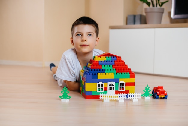 Um menino brinca com um kit de construção e constrói uma casa-grande para toda a família. construção de uma casa de família.