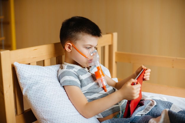 Um menino brinca em um tablet durante um procedimento de inalação pulmonar. covid19, coronavírus, pandemia.