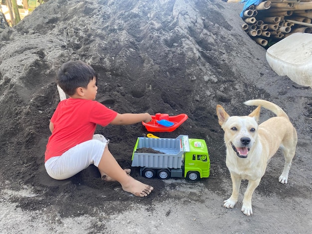 Um menino brincando com um caminhão de brinquedo ao lado de um monte de areia.