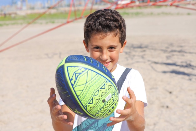 Um menino brincando com uma bola de rugby na praia