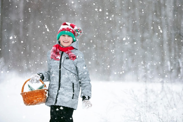 Um menino caminha na floresta de inverno com uma cesta de Natal