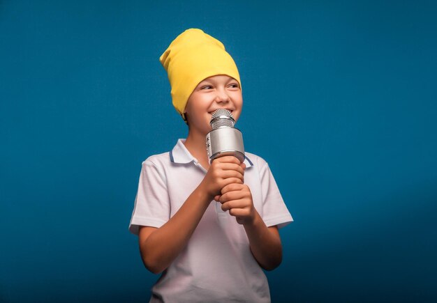 Um menino canta em um microfone em um fundo azul Um menino bonito em uma camiseta branca e shorts fica em um fundo azul e canta emocionalmente no microfone