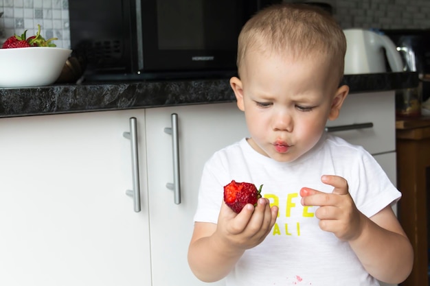 Um menino careca não está comendo morangos suculentos vermelhos de maneira organizada e apetitosa