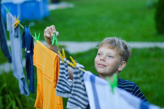 Um menino caucasiano feliz de 9 anos ajuda sua mãe a pendurar roupas Desenvolvimento de habilidades motoras finas por meio de atividades domésticas Foco seletivo