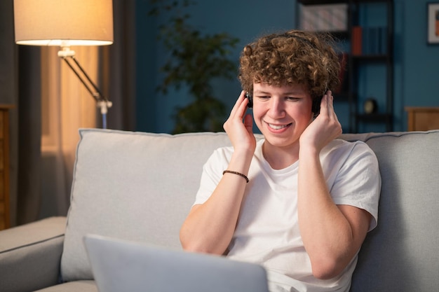 Um menino com cabelo encaracolado se senta em um sofá na sala de estar com um laptop no colo