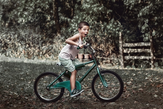 Um menino com cara engraçada andando em sua velha bicicleta rústica um menino andando em sua velha bicicleta no quintal