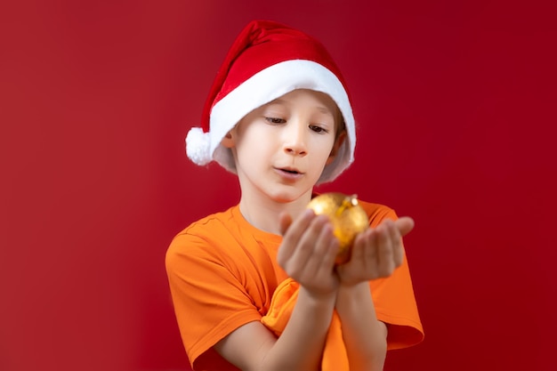 Um menino com chapéu de Papai Noel segura uma bola de Natal na palma das mãos à sua frente